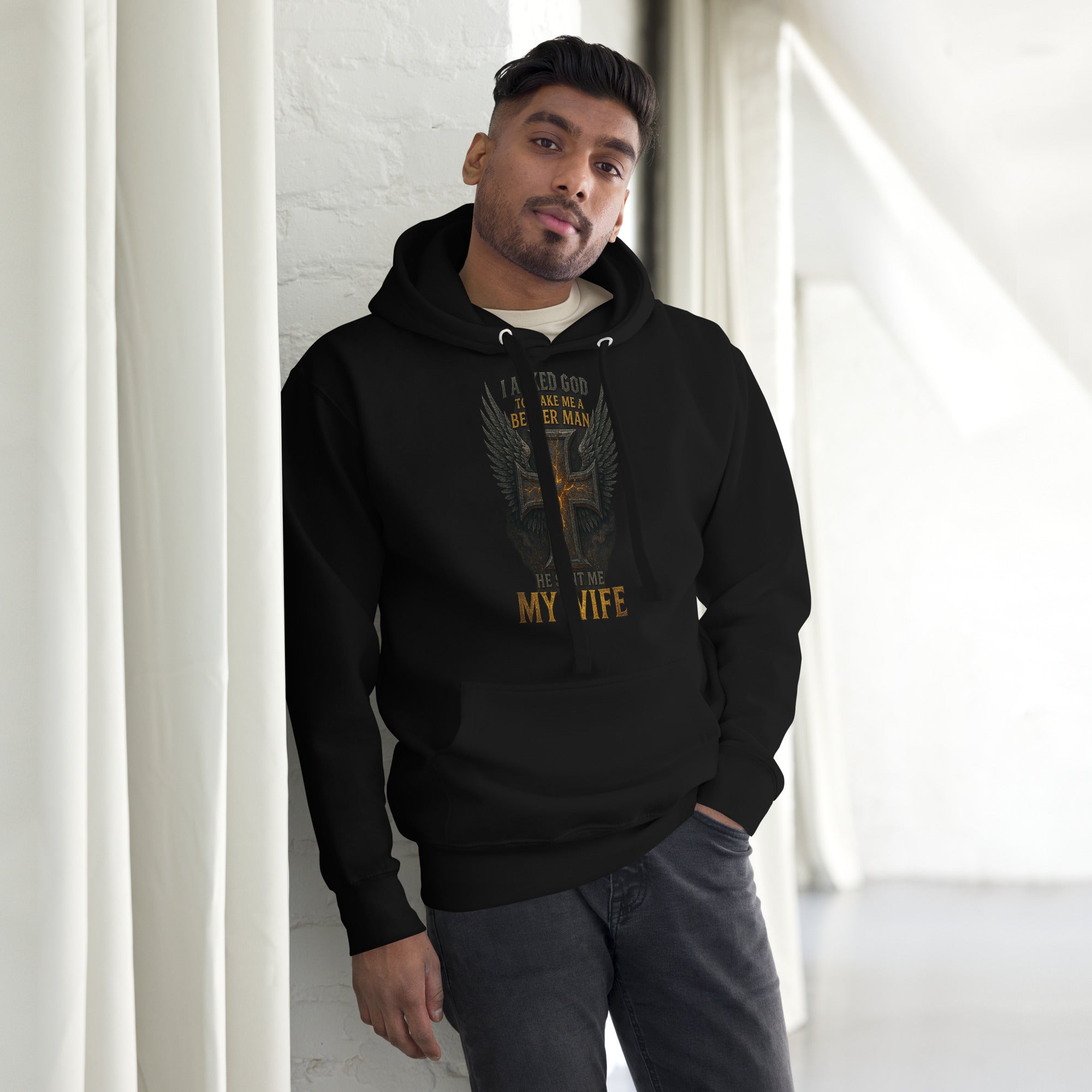 Black Christian hoodie with cross and wings design that reads “I asked God to make me a better man, He sent me my wife.”